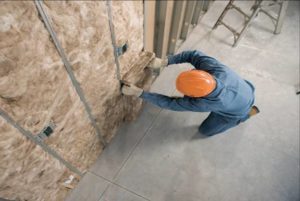 Overhead view of a technician in orange hard hat installing batt insulation in a wall.