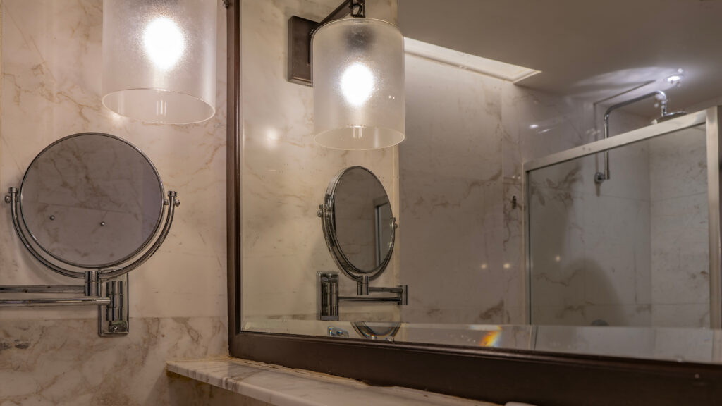 A bathroom mirror reflecting a smaller mirror and pendant light